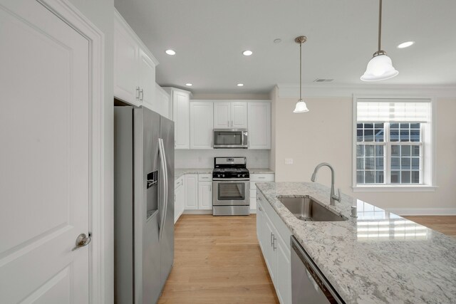 kitchen with pendant lighting, light wood finished floors, stainless steel appliances, white cabinetry, and a sink