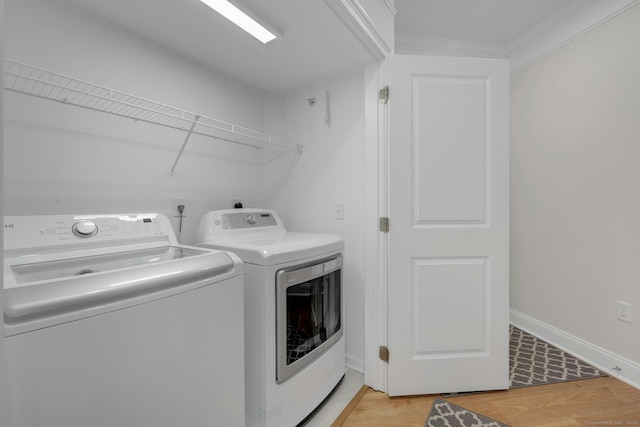 clothes washing area featuring washing machine and dryer, laundry area, baseboards, ornamental molding, and light wood-type flooring