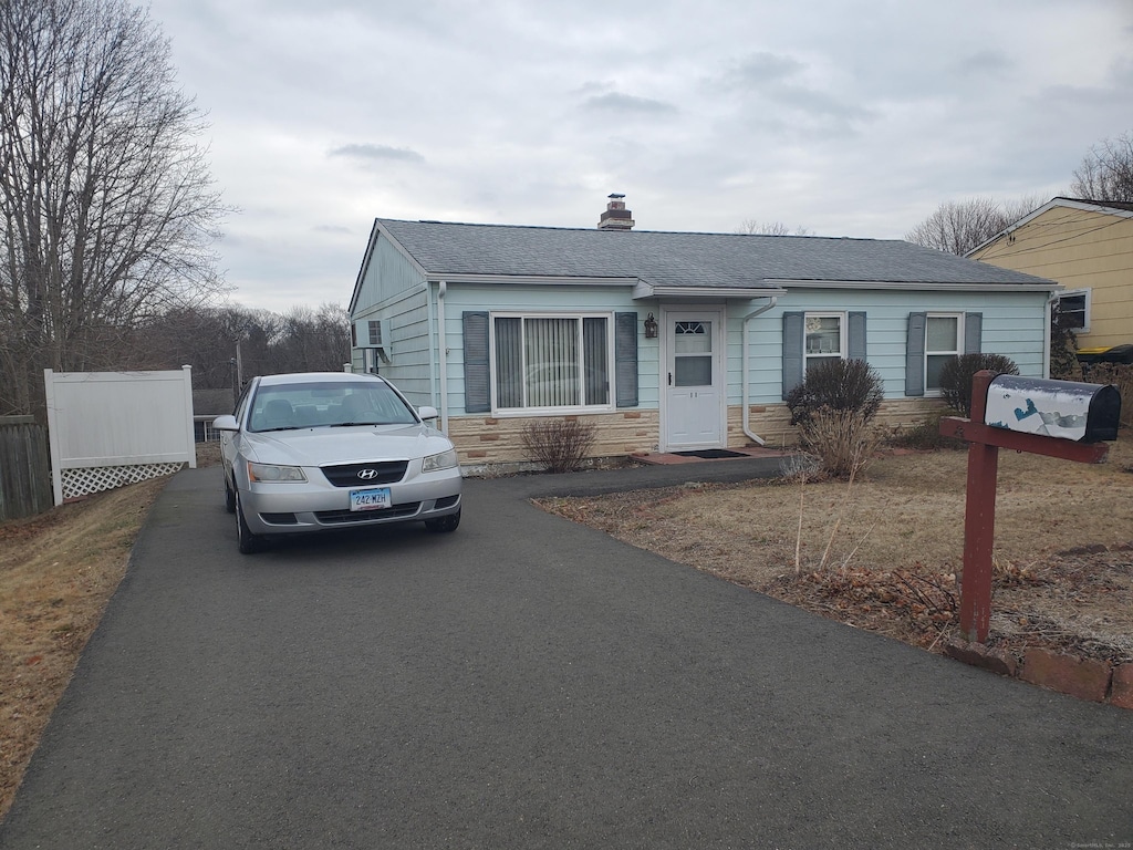 view of front of home featuring a chimney, a shingled roof, fence, stone siding, and driveway