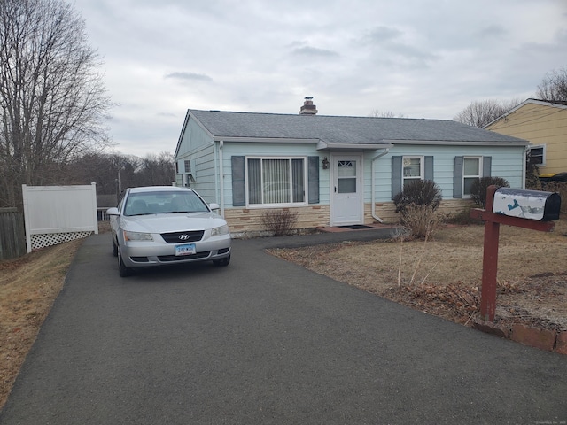 view of front of home featuring a chimney, a shingled roof, fence, stone siding, and driveway