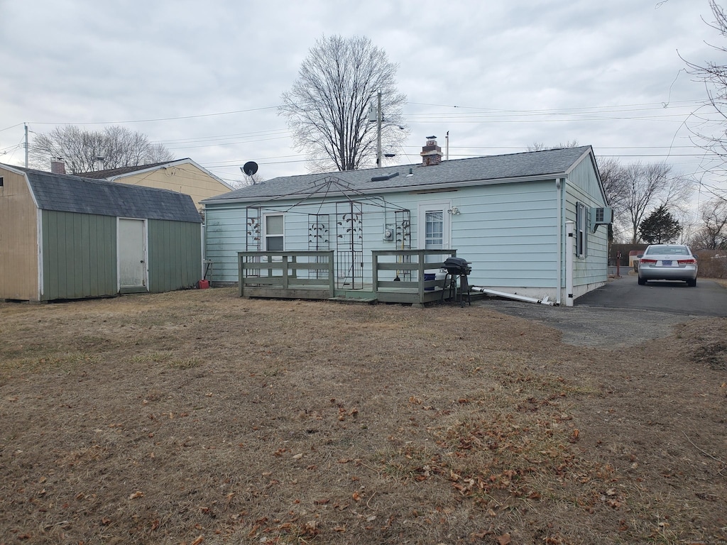 rear view of house with a storage shed, a chimney, roof with shingles, an outbuilding, and a wooden deck