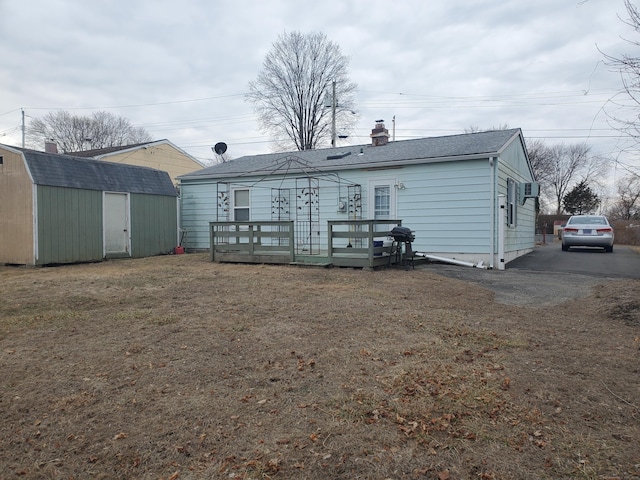 rear view of house with a storage shed, a chimney, roof with shingles, an outbuilding, and a wooden deck