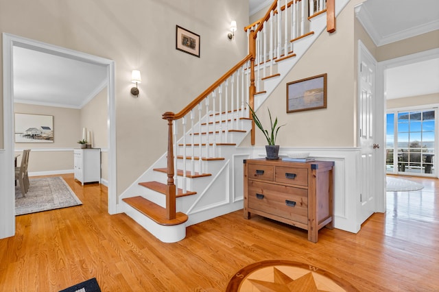 stairway with ornamental molding, a wainscoted wall, and wood finished floors