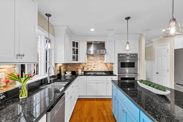 kitchen featuring white cabinets, blue cabinets, stainless steel appliances, wall chimney range hood, and a sink