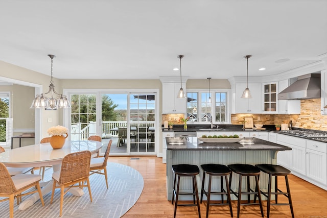 kitchen with light wood-style floors, wall chimney exhaust hood, white cabinets, and a sink