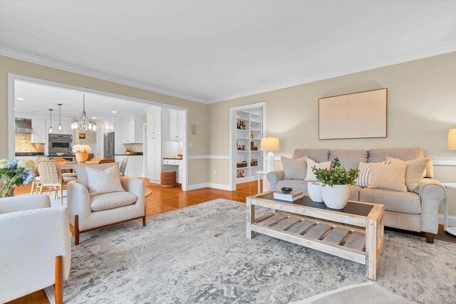 living room with a chandelier, ornamental molding, light wood-style flooring, and baseboards