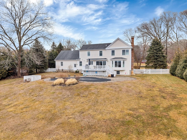 rear view of house with a deck, a chimney, a fenced backyard, and a lawn