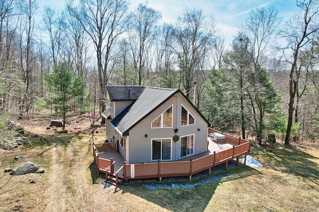 back of property featuring a wooden deck, a view of trees, a lawn, and a shingled roof