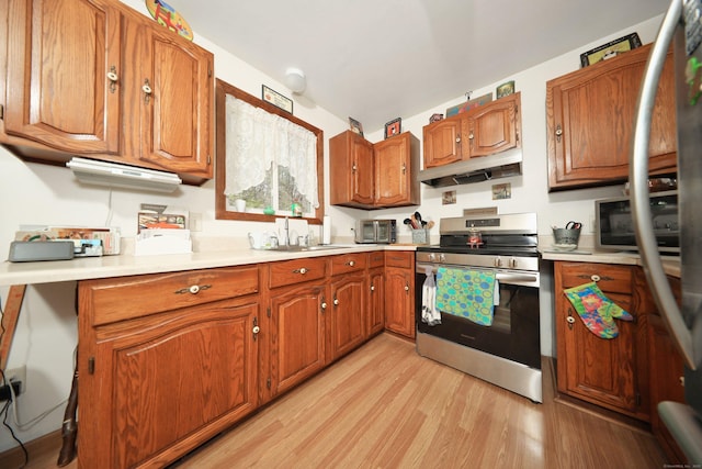 kitchen with brown cabinetry, a sink, stainless steel range with electric stovetop, light wood-style floors, and under cabinet range hood