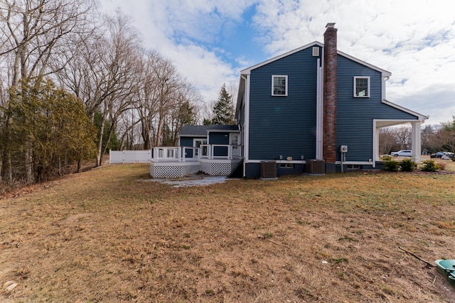 rear view of property featuring a deck, central AC unit, a lawn, and a chimney