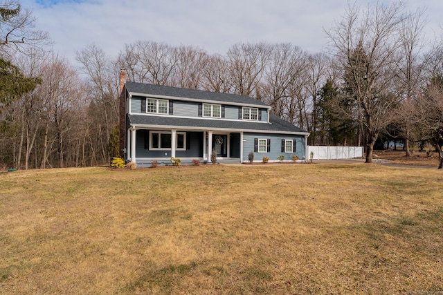 view of front facade with a shingled roof, a front lawn, fence, and a chimney