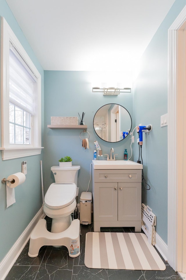 half bathroom with vanity, toilet, and baseboards