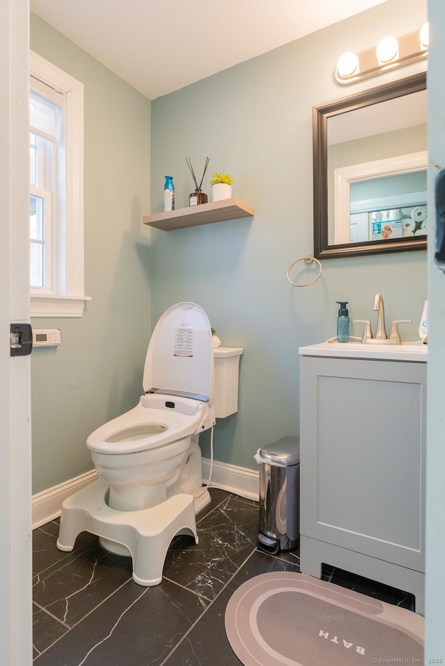 half bath featuring baseboards, toilet, marble finish floor, and vanity