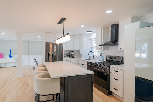 kitchen featuring tasteful backsplash, appliances with stainless steel finishes, white cabinetry, and wall chimney range hood