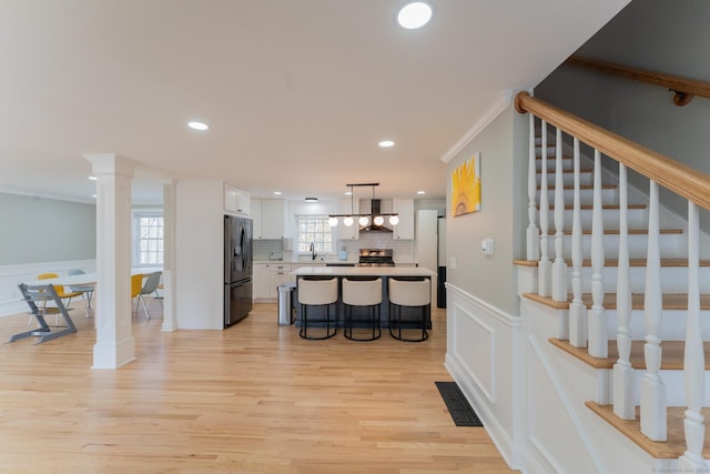 kitchen featuring visible vents, white cabinetry, a breakfast bar area, wall chimney range hood, and black refrigerator with ice dispenser