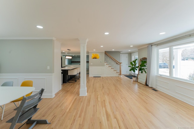 living area with stairway, visible vents, light wood finished floors, decorative columns, and a decorative wall