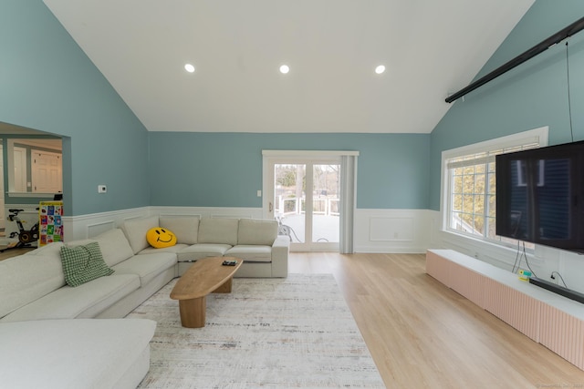 living room with lofted ceiling, light wood-style flooring, a healthy amount of sunlight, and a wainscoted wall