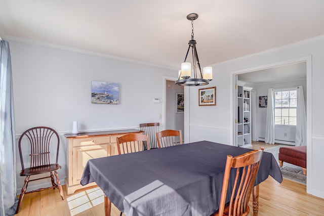 dining area with light wood-style floors, a chandelier, and ornamental molding