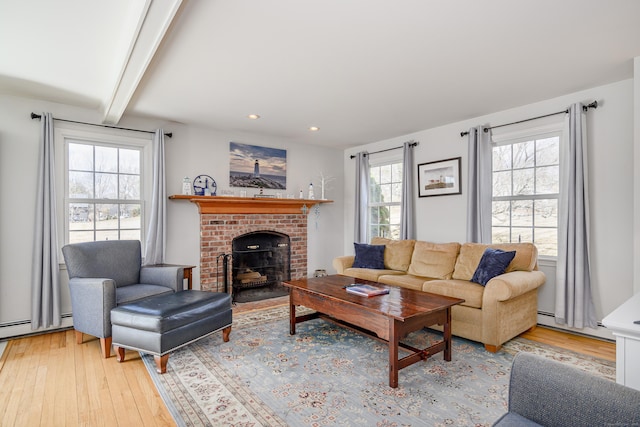 living area featuring beamed ceiling, light wood-type flooring, recessed lighting, a fireplace, and a baseboard radiator