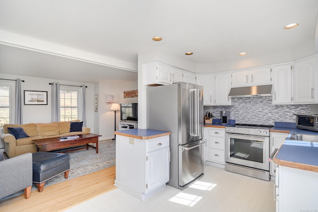 kitchen featuring backsplash, under cabinet range hood, open floor plan, appliances with stainless steel finishes, and white cabinets