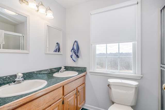 bathroom featuring double vanity, a shower with shower door, toilet, and a sink