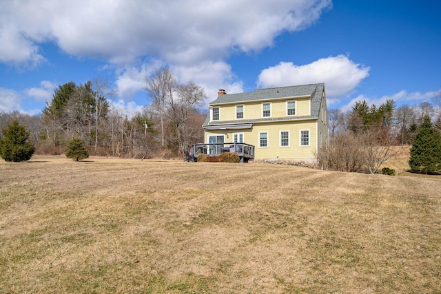 rear view of property with a deck, a chimney, and a yard