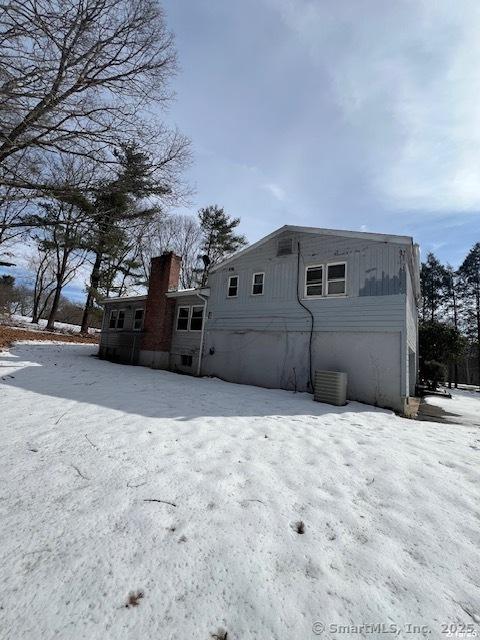 view of snow covered exterior featuring central AC unit and an attached garage