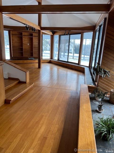 unfurnished living room featuring lofted ceiling with beams, wood finished floors, and a wealth of natural light