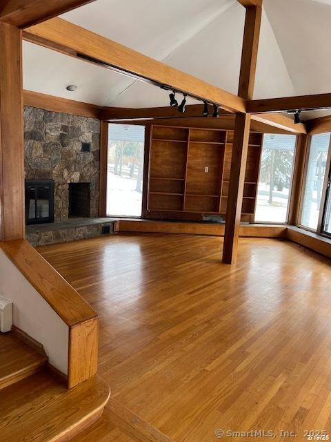 unfurnished living room featuring lofted ceiling with beams, a wealth of natural light, a fireplace, and wood finished floors