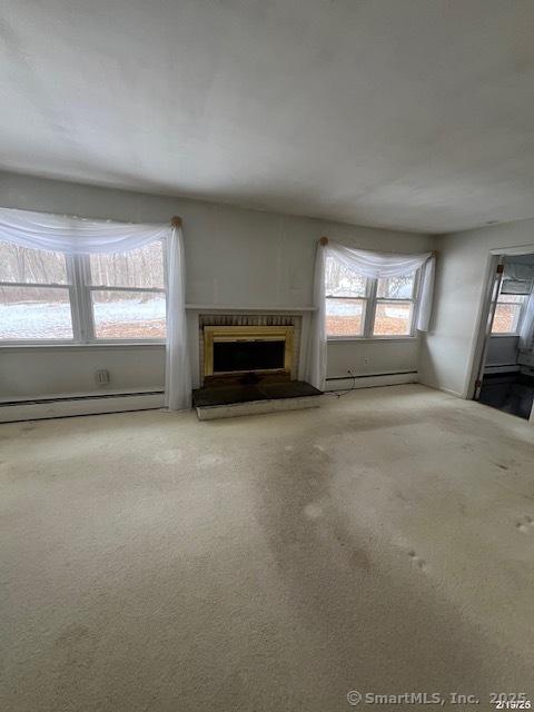 unfurnished living room featuring carpet, baseboard heating, and a fireplace with raised hearth