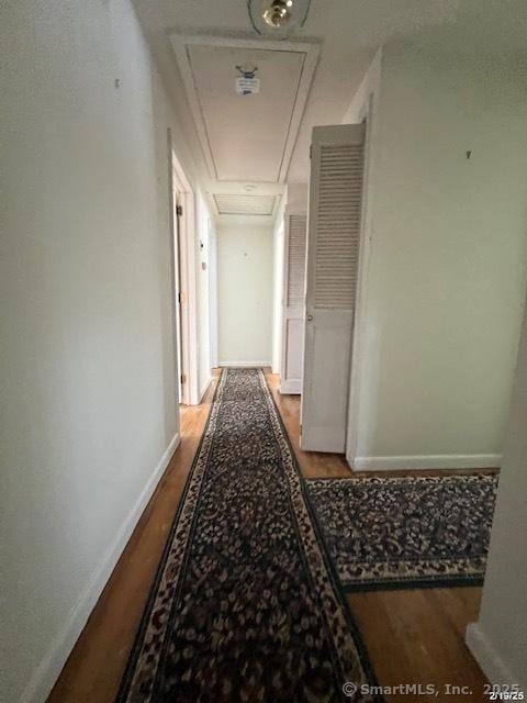 corridor featuring attic access, baseboards, and wood finished floors