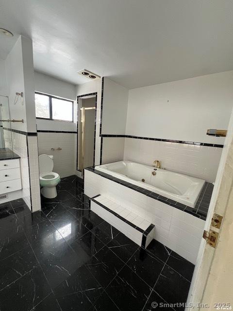 full bathroom featuring a garden tub, tile walls, toilet, a stall shower, and vanity