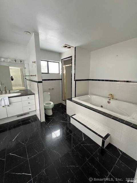 bathroom featuring toilet, vanity, visible vents, tile walls, and a jetted tub