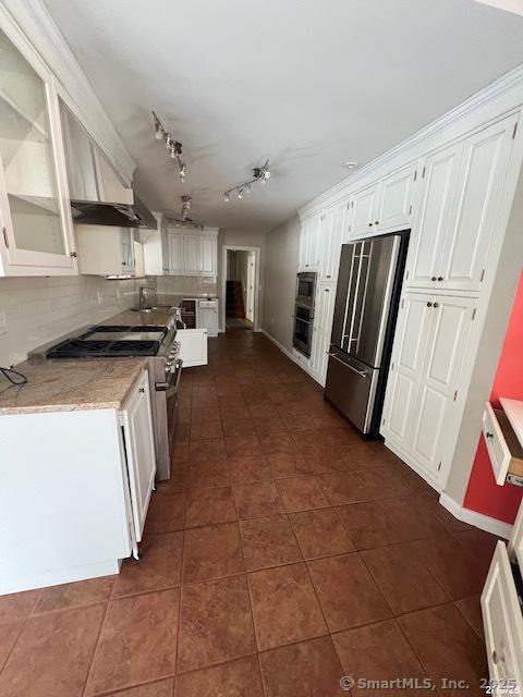 kitchen with tasteful backsplash, high end appliances, dark tile patterned flooring, glass insert cabinets, and white cabinetry