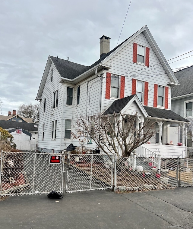 view of front of property featuring roof with shingles, a fenced front yard, a chimney, and a gate