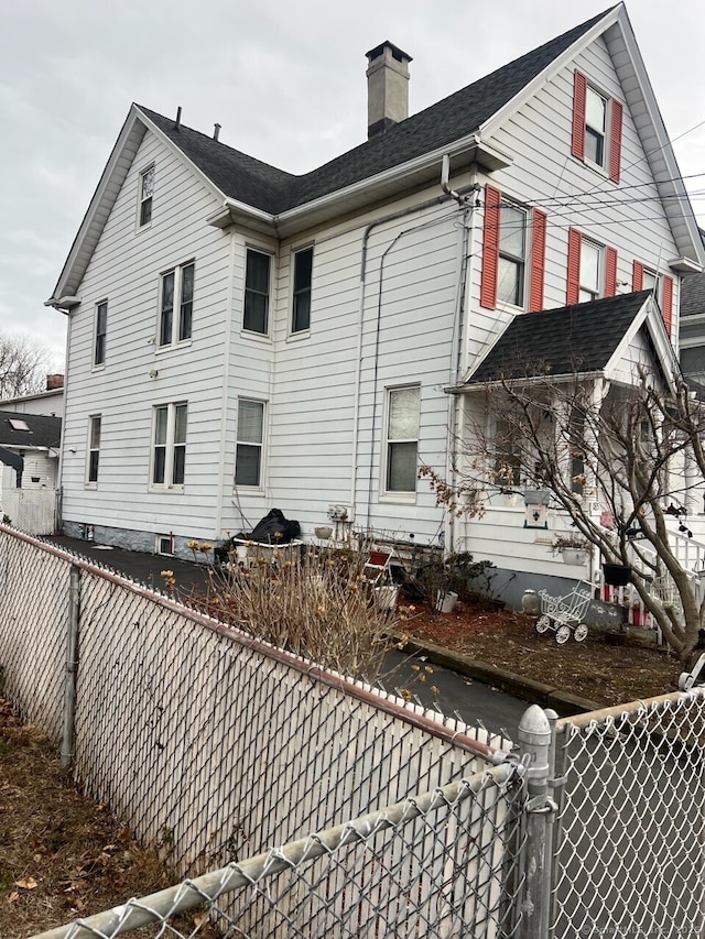 back of house featuring a chimney, a fenced backyard, and a gate