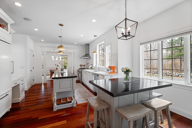 kitchen featuring dark countertops, an inviting chandelier, a center island, and wall chimney exhaust hood