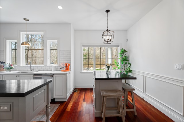 kitchen featuring stainless steel dishwasher, dark wood-style floors, a sink, a chandelier, and a kitchen island