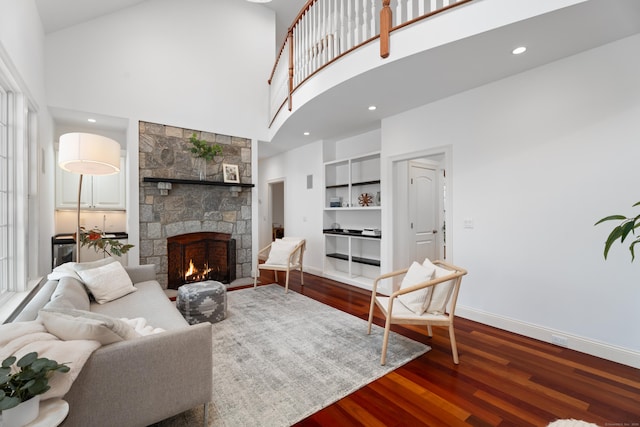 living room featuring dark wood finished floors, a stone fireplace, a high ceiling, and baseboards