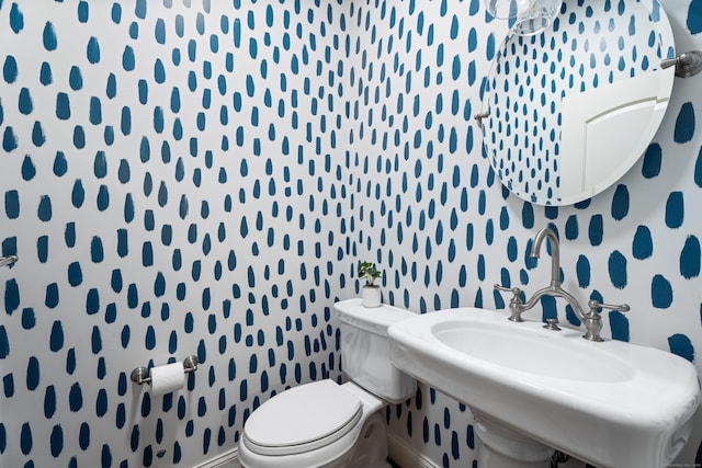 bathroom with toilet, a sink, wallpapered walls, and baseboards
