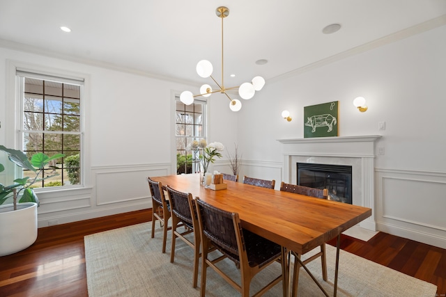 dining space with a high end fireplace, wood finished floors, ornamental molding, and wainscoting