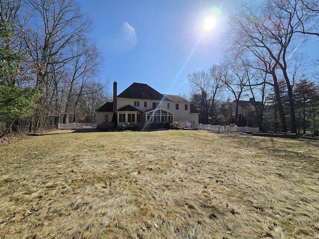 rear view of property featuring a chimney, a yard, and fence