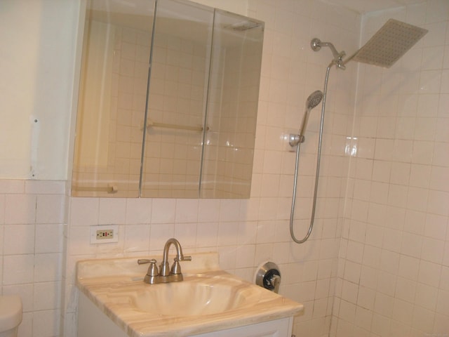 bathroom featuring tile walls, a tile shower, vanity, and toilet