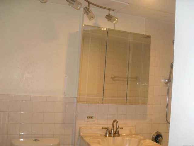 bathroom with toilet, a sink, a shower, and tile walls