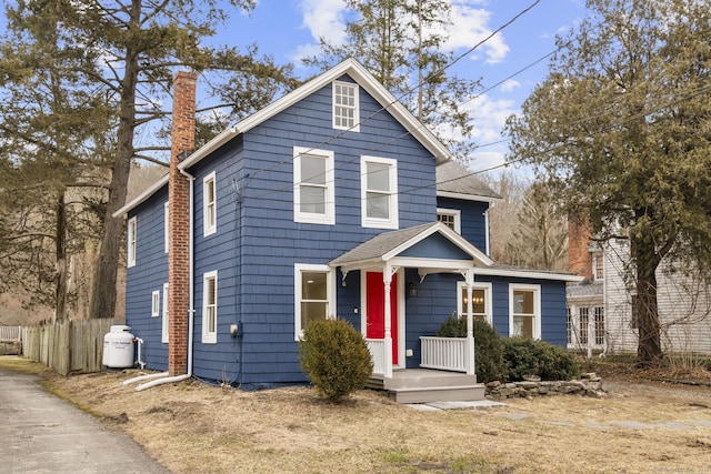 view of front of home with a shingled roof, a chimney, and fence