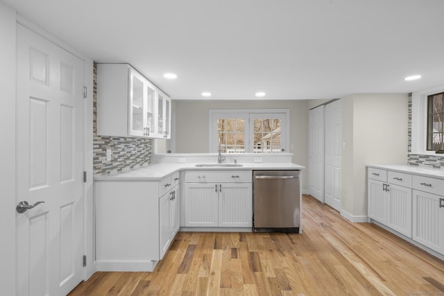 kitchen featuring light countertops, stainless steel dishwasher, glass insert cabinets, a sink, and light wood-type flooring