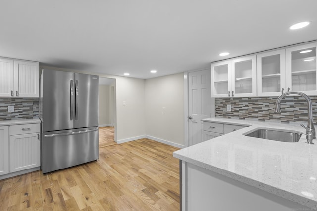 kitchen featuring white cabinets, a sink, freestanding refrigerator, and light wood-style floors