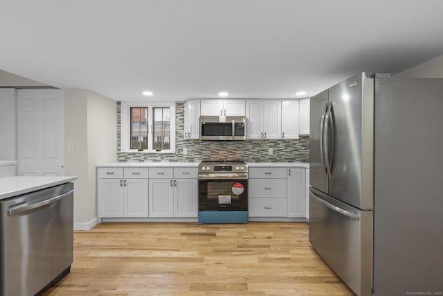 kitchen featuring light wood finished floors, decorative backsplash, stainless steel appliances, light countertops, and white cabinetry