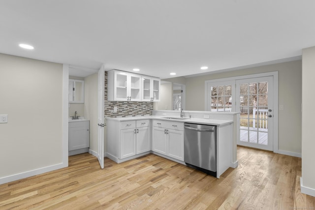 kitchen featuring white cabinets, dishwasher, backsplash, a peninsula, and a sink