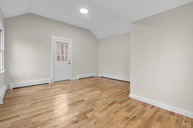 empty room with lofted ceiling, light wood finished floors, and a baseboard heating unit